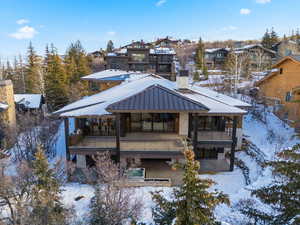 Snow covered rear of property with a chimney, a sunroom, a metal roof, a standing seam roof, and a wooden deck