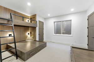Unfurnished bedroom with light colored carpet, recessed lighting, and wooden walls
