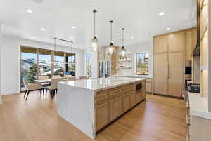 Kitchen with light stone counters, light brown cabinets, light wood-style flooring, open shelves, and decorative light fixtures