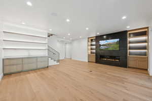 Unfurnished living room featuring built in shelves, stairs, light wood-style floors, recessed lighting, and a large fireplace