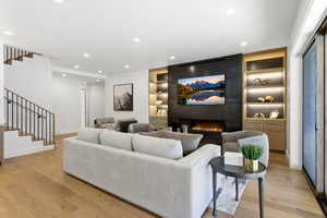 Living room featuring built in shelves, stairway, a large fireplace, light wood-type flooring, and recessed lighting