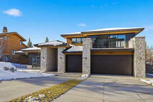 Contemporary home with a balcony, concrete driveway, stone siding, and a garage