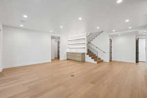 Unfurnished living room with recessed lighting, light wood-style flooring, stairway, and built in features