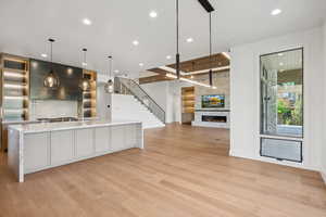 Kitchen featuring hanging light fixtures, a fireplace, a spacious island, light stone countertops, and light wood finished floors