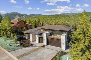 View of front of house featuring driveway, stone siding, an attached garage, a mountain view, and a view of trees