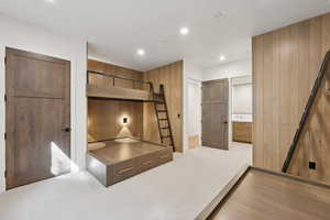 Unfurnished bedroom featuring wooden walls, light carpet, a barn door, recessed lighting, and connected bathroom