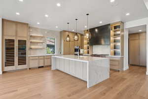 Kitchen featuring open shelves, light stone counters, beverage cooler, hanging light fixtures, and recessed lighting