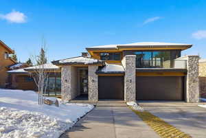 Contemporary home featuring concrete driveway, stone siding, an attached garage, and a balcony