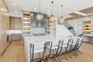 Kitchen with light stone countertops, pendant lighting, open shelves, a large island with sink, and a kitchen bar