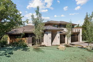 Prairie-style house featuring stone siding, a front yard, driveway, a balcony, and an attached garage