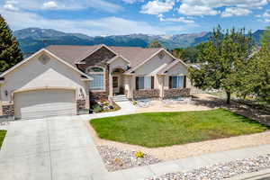 View of front of home with stone siding, a mountain view, a garage, driveway, and a front yard