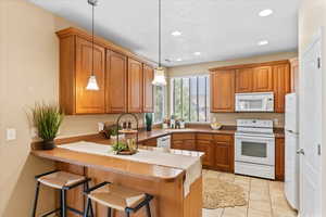 Kitchen with white appliances, a kitchen bar, pendant lighting, light tile patterned floors, and recessed lighting