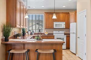 Kitchen featuring white appliances, a breakfast bar, a peninsula, brown cabinetry, and light tile patterned flooring