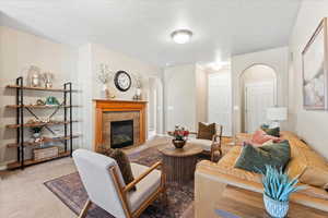 Living room with light carpet, a tile fireplace, arched walkways, and a textured ceiling
