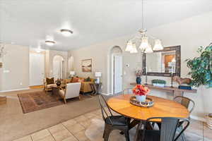 Dining area with light carpet, arched walkways, light tile patterned floors, and a chandelier