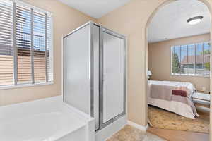 Ensuite bathroom featuring healthy amount of natural light, a bath, and a stall shower