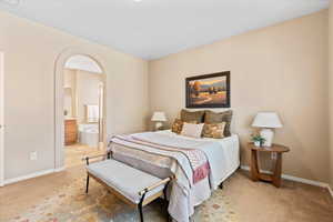 Bedroom featuring light carpet, arched walkways, and ensuite bath