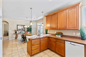 Kitchen featuring white dishwasher, a peninsula, light tile patterned floors, and decorative light fixtures