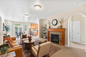 Living area featuring a tiled fireplace, light colored carpet, and a textured ceiling