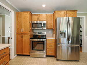 Kitchen with stainless steel appliances, ornamental molding, light countertops, light tile patterned floors, and brown cabinetry