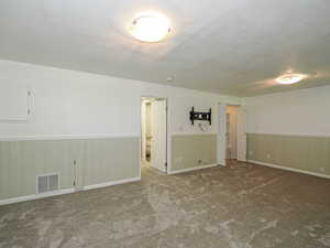 Family room or bedroom room featuring a textured ceiling, carpet flooring, and a wainscoted wall