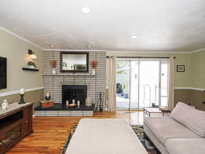 Living room featuring crown molding, wood finished floors, a brick fireplace, a textured ceiling, and recessed lighting