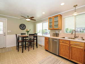 Kitchen with light countertops, ornamental molding, glass insert cabinets, stainless steel dishwasher, and brown cabinetry