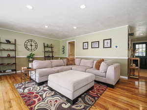 Living room with crown molding, wood finished floors, a textured ceiling, and recessed lighting