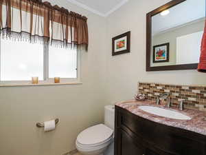 Half bathroom with tasteful backsplash, ornamental molding, and vanity
