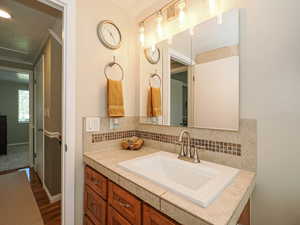 Half bathroom featuring vanity, backsplash, and dark wood-style flooring
