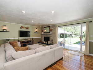 Living area with ornamental molding, a textured ceiling, wood finished floors, a fireplace, and recessed lighting