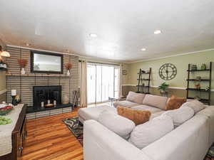 Living room with a textured ceiling, wood finished floors, a fireplace, crown molding, and recessed lighting