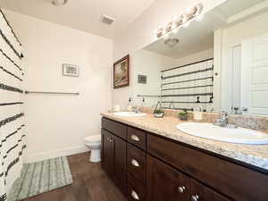 Full bath with dark wood finished floors, double vanity, and curtained shower