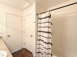Full bathroom with double vanity, shower / bath combination with curtain, and dark wood-style flooring
