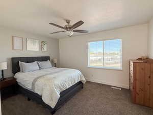 Bedroom with dark carpet, a ceiling fan, and a textured ceiling