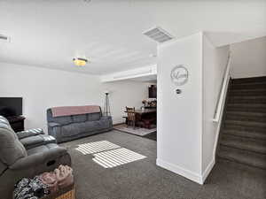Living room featuring a textured ceiling, carpet flooring, and stairs