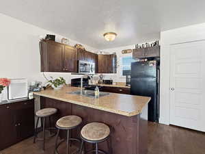 Kitchen featuring dark brown cabinetry, dark wood-style flooring, black appliances, a peninsula, and a textured ceiling