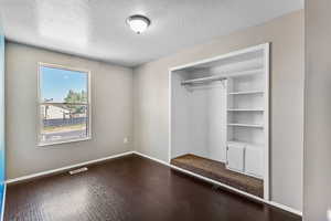Unfurnished bedroom featuring a textured ceiling, dark wood-type flooring, and a closet