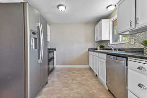 Kitchen featuring stainless steel appliances, dark countertops, white cabinets, and decorative backsplash