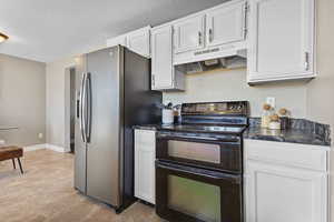 Kitchen with double oven range, white cabinets, under cabinet range hood, stainless steel refrigerator with ice dispenser, and a textured ceiling