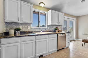 Kitchen featuring decorative backsplash, white cabinetry, stainless steel dishwasher, and a textured ceiling