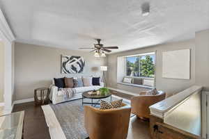Living area featuring a ceiling fan, a textured ceiling, and dark wood finished floors
