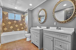 Full bath featuring bathtub / shower combination, two vanities, light tile patterned flooring, crown molding, and recessed lighting