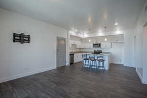 Kitchen with white cabinets, dark wood-style floors, hanging light fixtures, a breakfast bar area, and recessed lighting