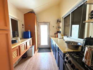 Kitchen featuring open shelves, light countertops, blue cabinetry, stainless steel gas range, and light wood-type flooring