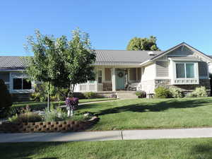 View of front of home with stone siding, covered porch, a front lawn, and a metal roof