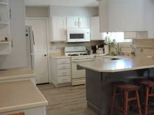 Kitchen with a peninsula, white cabinetry, light countertops, and a breakfast bar area