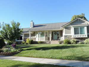 View of front of property featuring stone siding, covered porch, a front yard, a metal roof, and a chimney