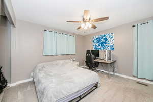 Bedroom with light colored carpet, ceiling fan, and an office area
