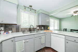 Kitchen featuring gray cabinetry, dishwasher, light countertops, tasteful backsplash, and a peninsula